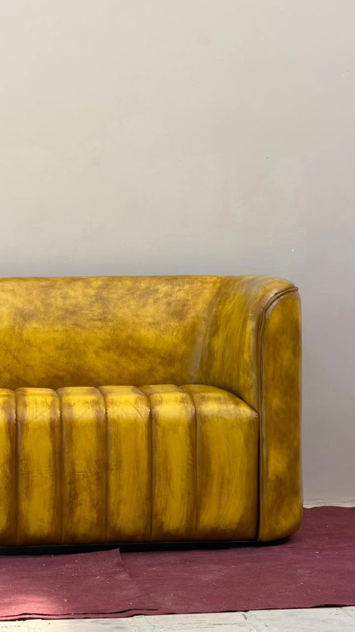 Yellow leather sofa against a plain wall with a red rug on the floor.